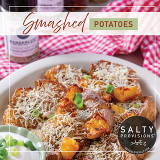 Plate of smashed potatoes with cheese and green onions on a table with 'Salty Provisions' branding.